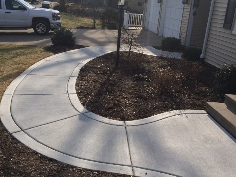 Concrete sidewalk connecting driveway with entrance of house.